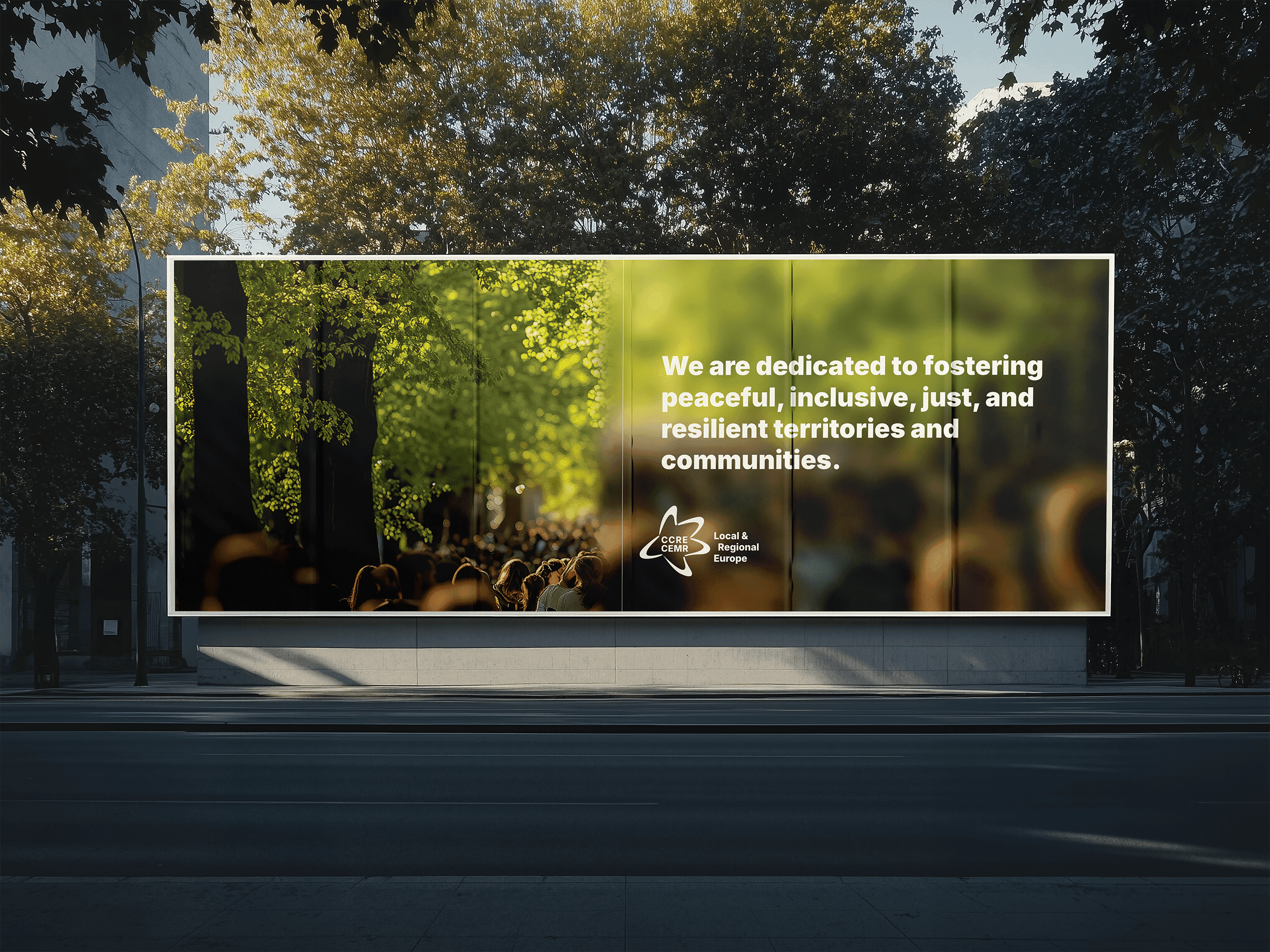 A CEMR brand campaign billboard on a tree-lined street, reading “We are dedicated to fostering peaceful, inclusive, just, and resilient territories and communities”
