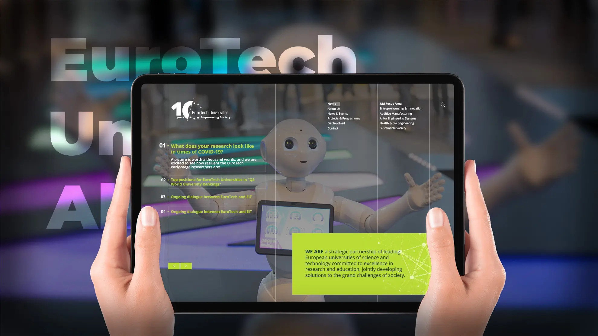 Hands holding a tablet showing the EuroTech Universities website, with a humanoid robot pictured on the homepage